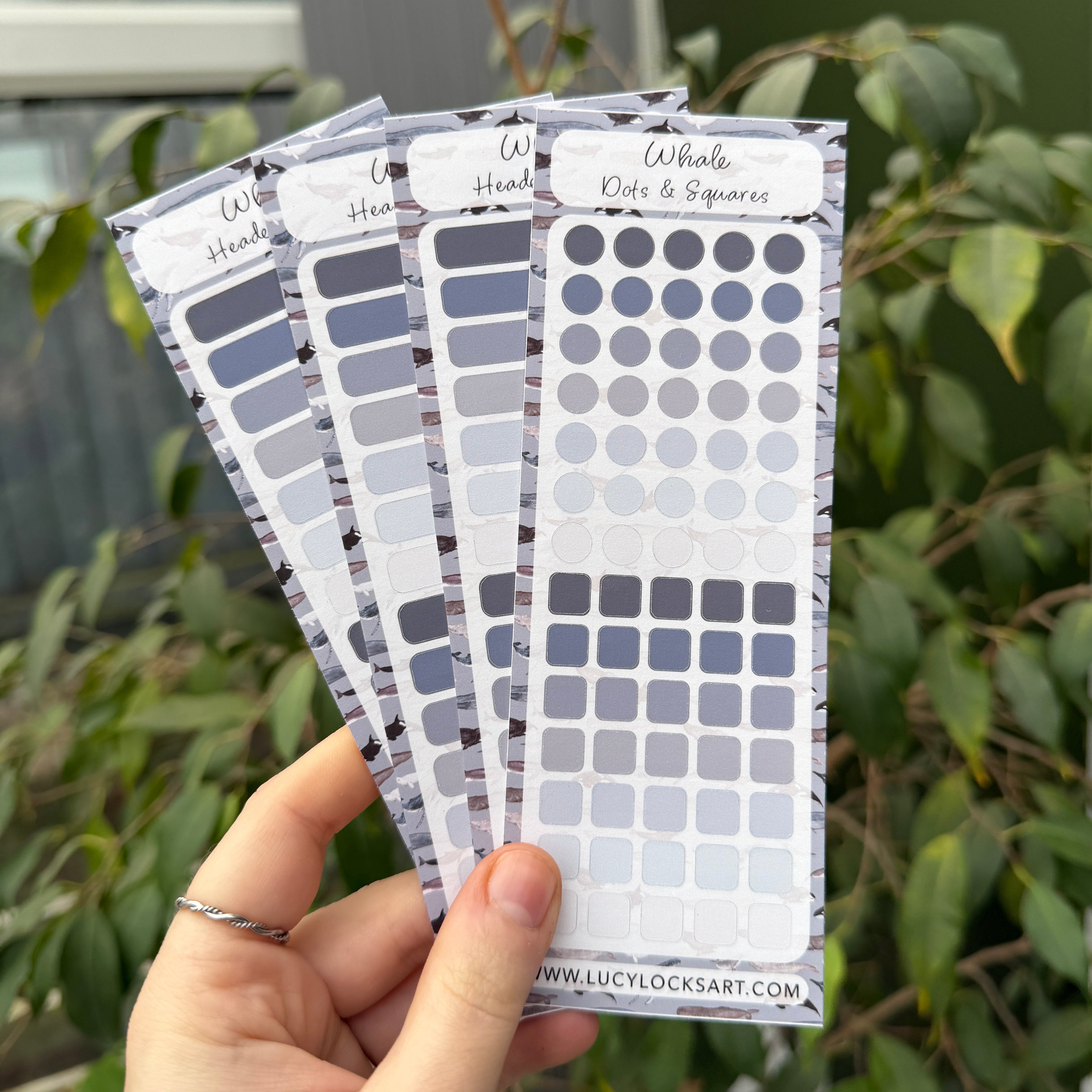 Hand holding a set of gray color journal stickers with a blurred green plant background