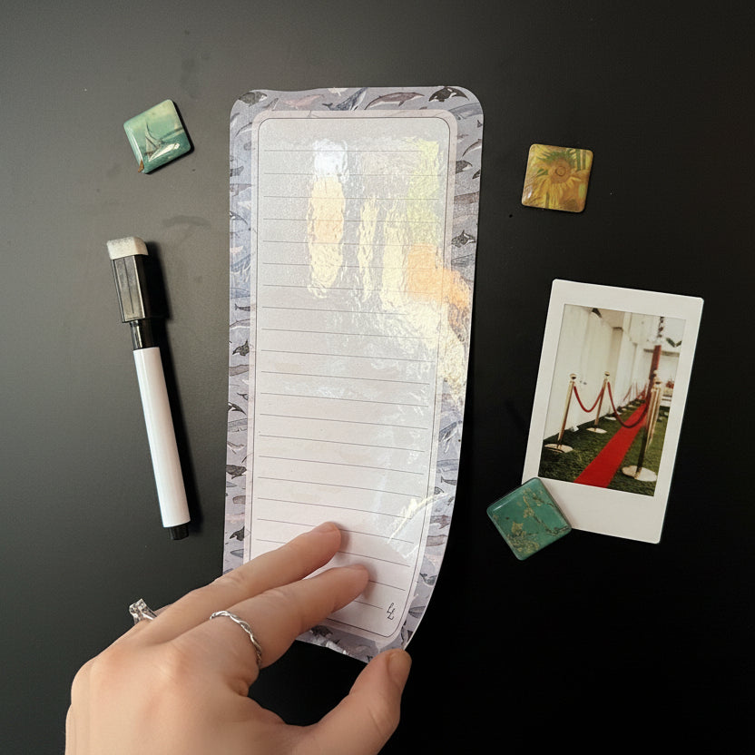 MAgnetic list with lines held by a hand on a magnetic surface with decorative items.
