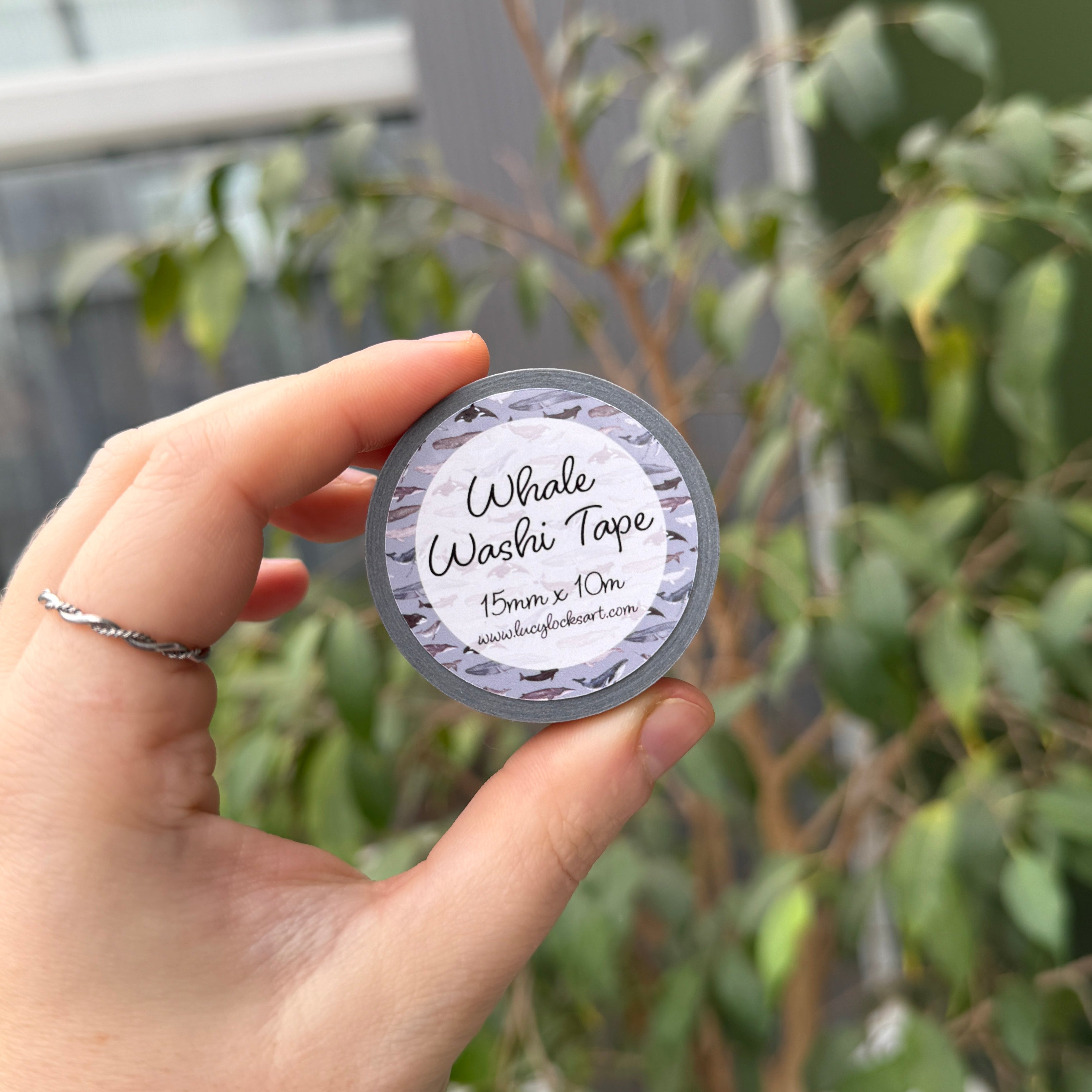 Hand holding a reel of whale printed washi tape with a label, outdoors.